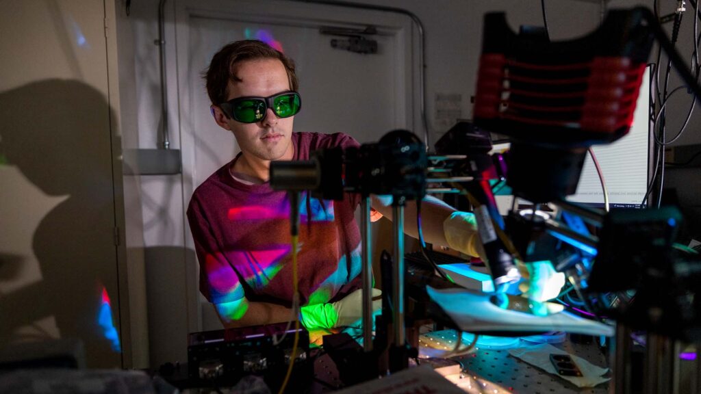 A student works in a dark laboratory at a lab bench using a laser