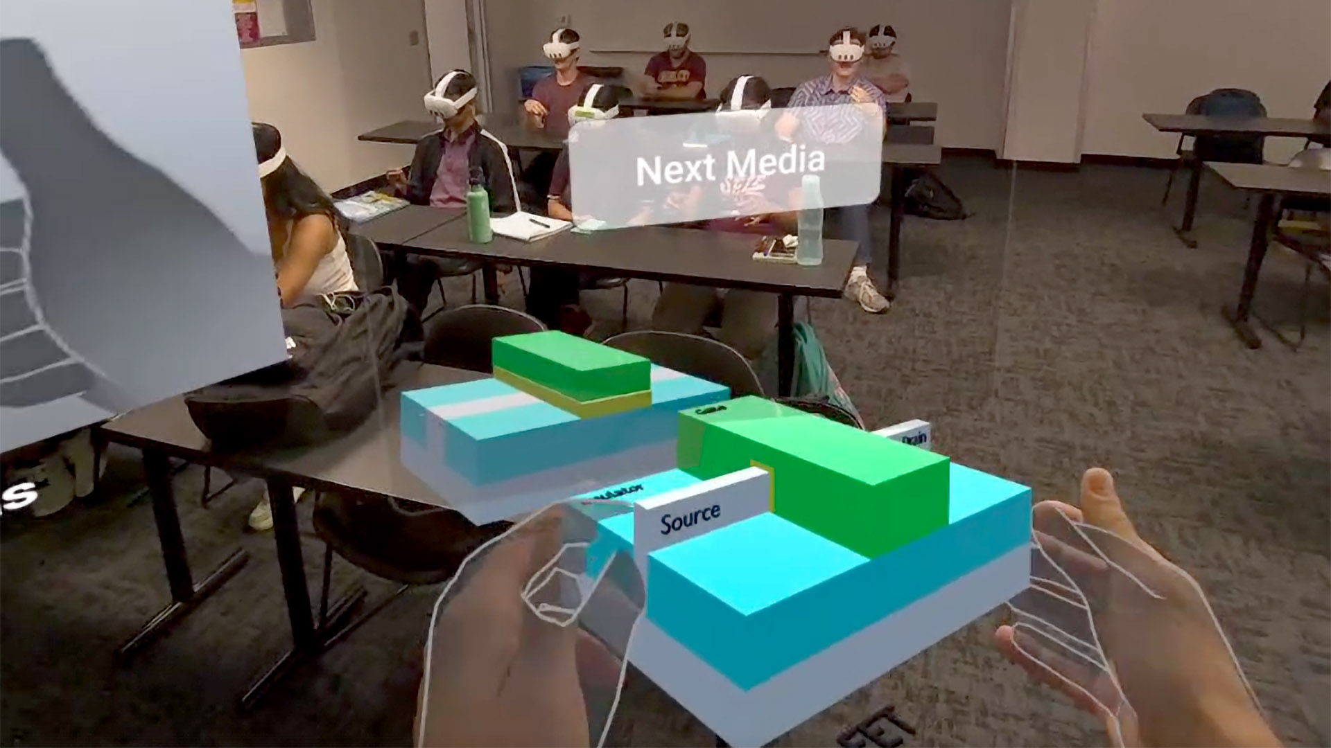 Students wearing VR headsets sit in a classroom, with virtual hands interacting with a 3D model labeled "Source" projected in the foreground.