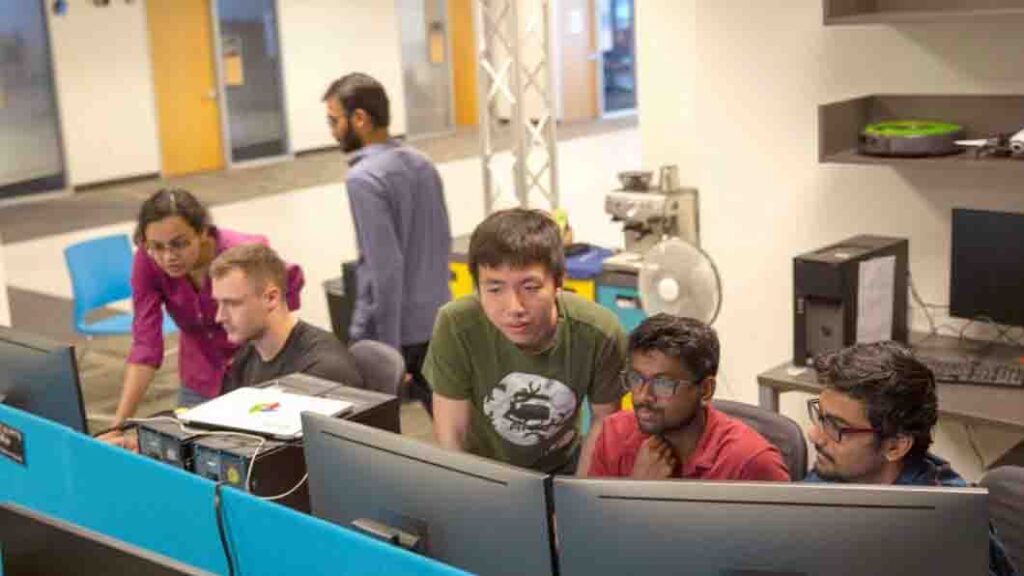 A diverse group of professionals collaborating at computers in a modern office environment.