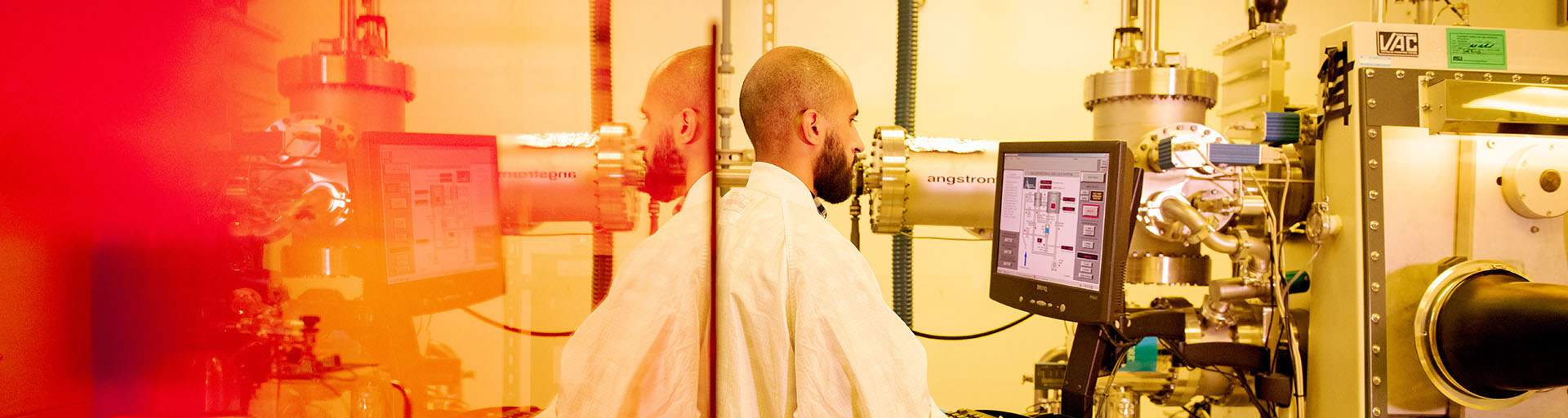 A man in a lab coat is focused on his work at a computer in a laboratory setting.